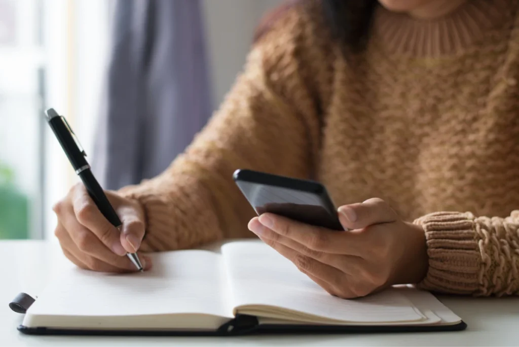 Writing notes while checking a phone.