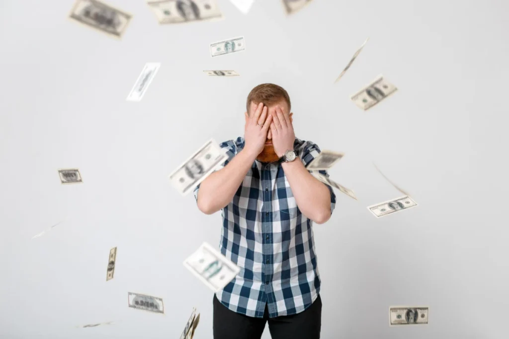 Man covering face as money falls.