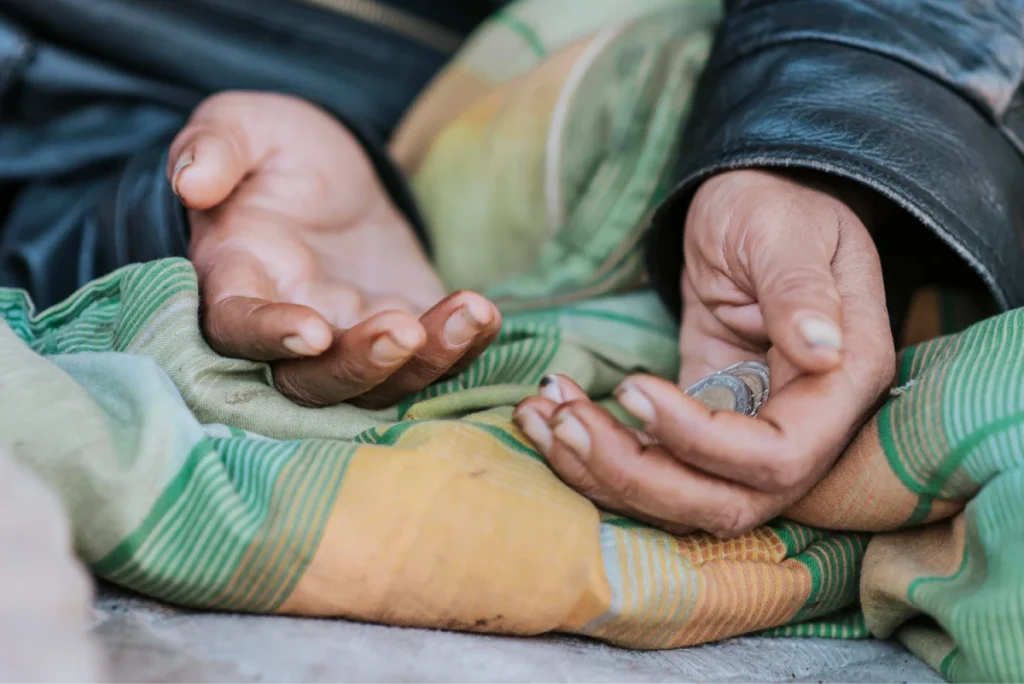 Hands holding coins while sitting on the ground.