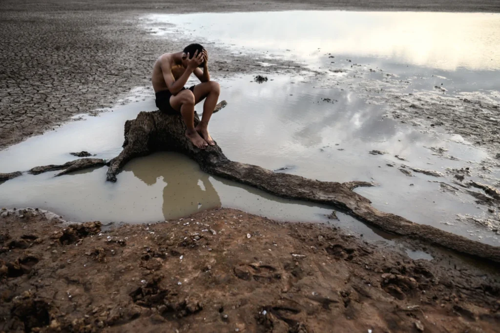 Person sitting on a dry, cracked land, holding head in despair.