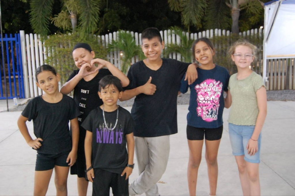 Group of six children smiling and posing together outdoors, representing joy and togetherness.