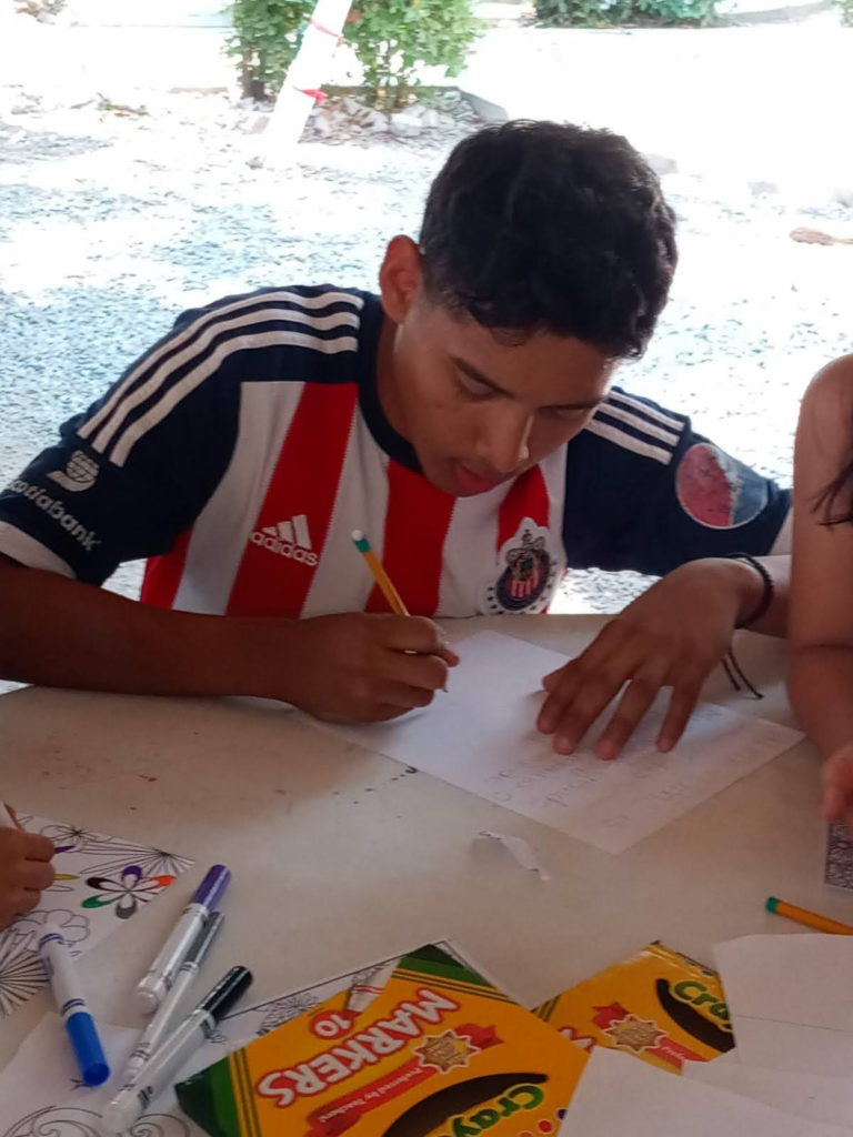 Teenager focused on drawing and coloring, sitting at a table with markers, representing concentration and creativity.