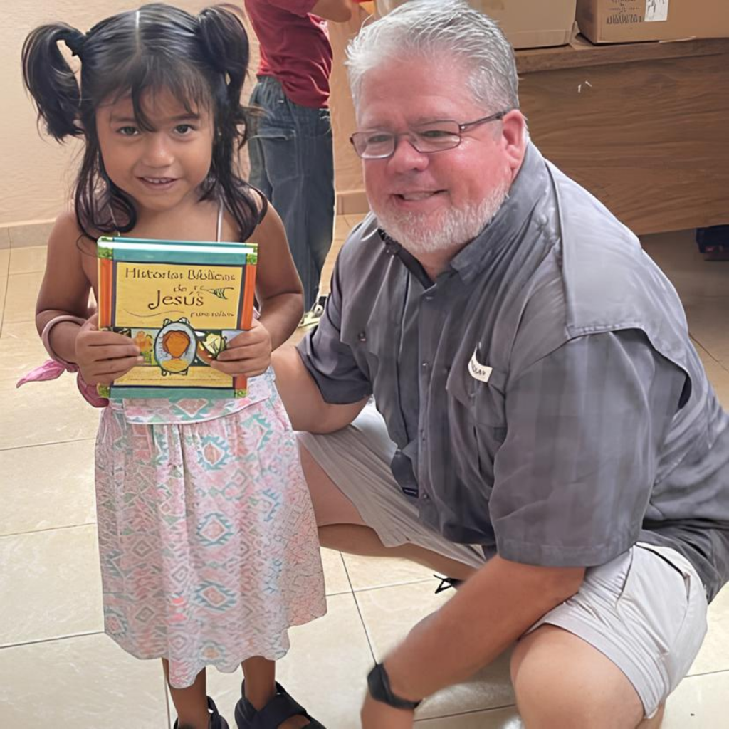 Young girl holding a children's book with an adult kneeling beside her, smiling warmly.