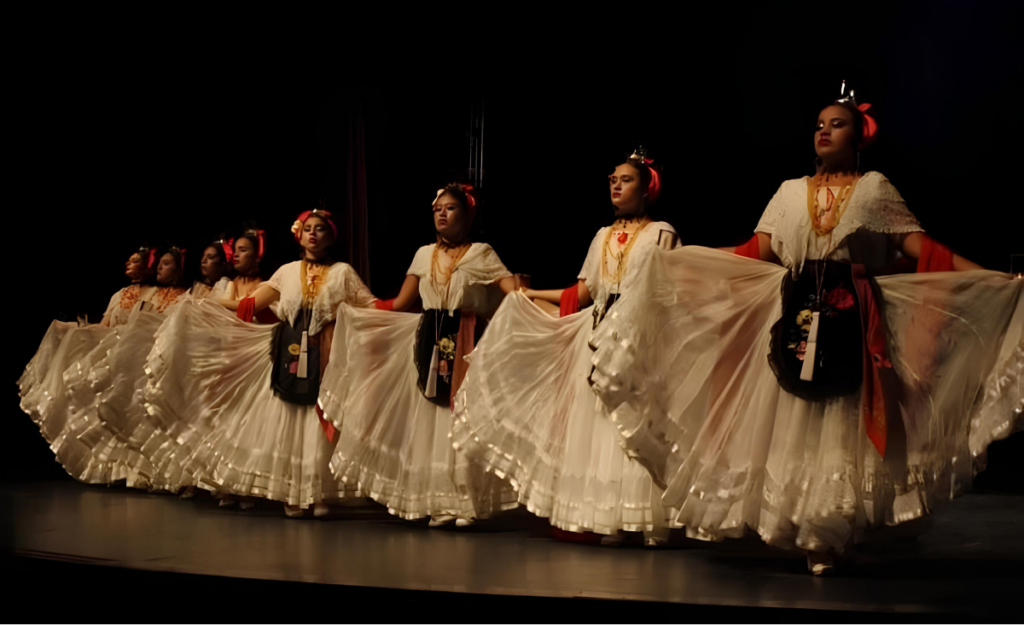 Traditional dancers performing on stage in white dresses with flowing skirts.